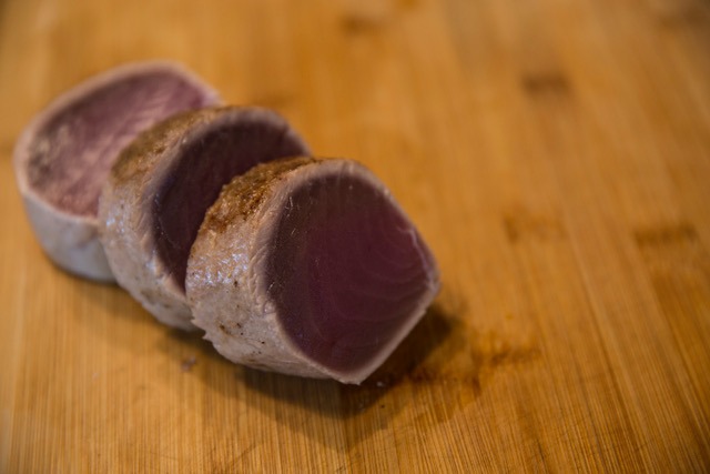 Three slices of seared ahi on a wooden cutting board